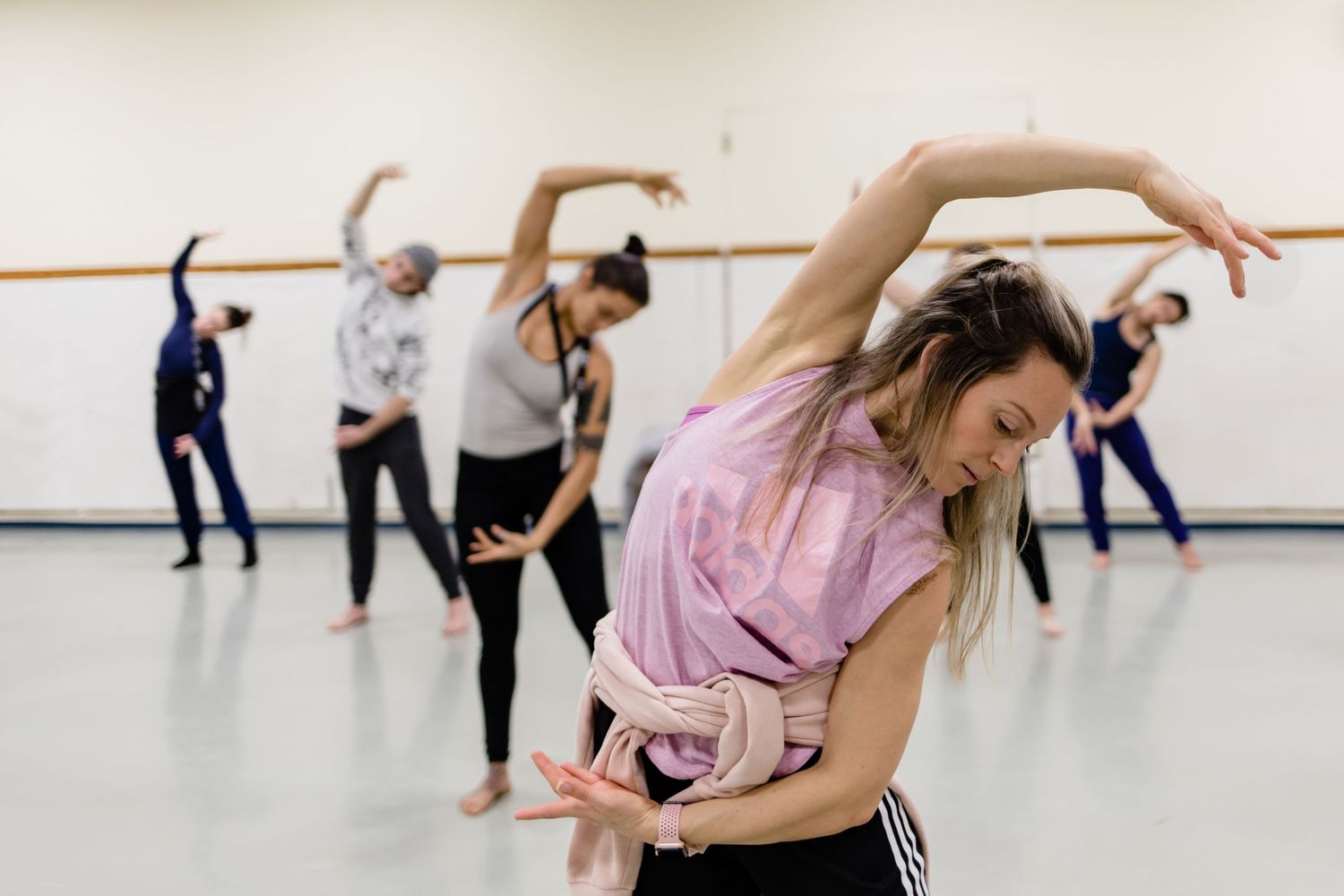 Dance students practice expressive movements in a bright studio with ballet barre and mirrored wall.