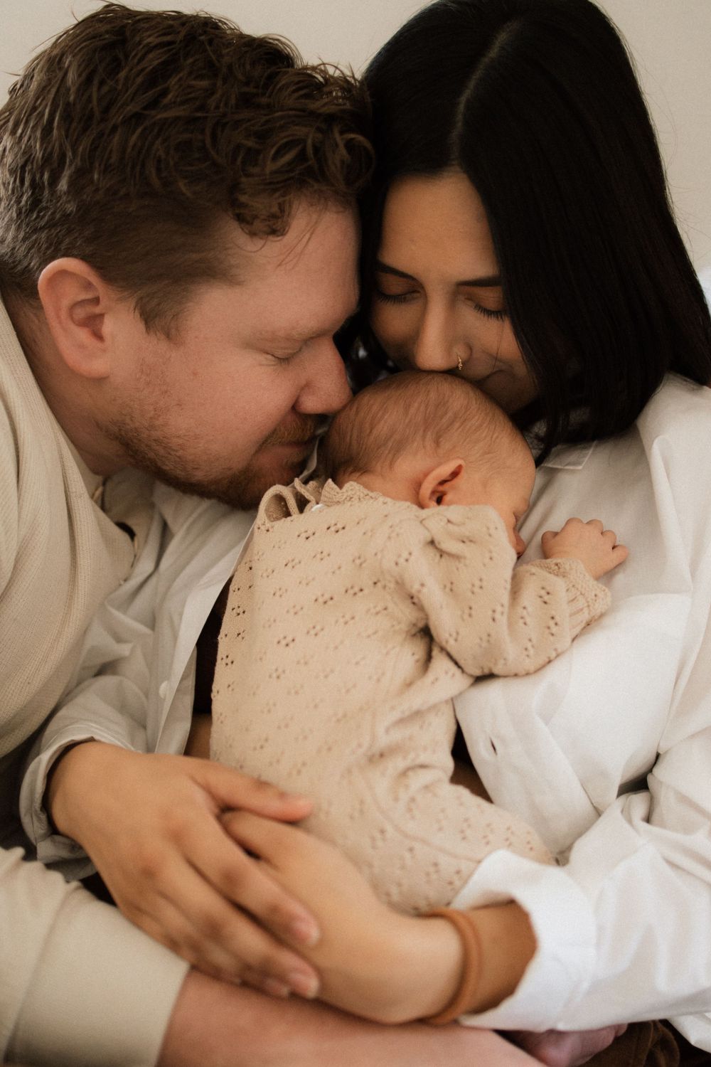 A family cuddles their newborn baby wearing a cream knit sweater in an intimate portrait.