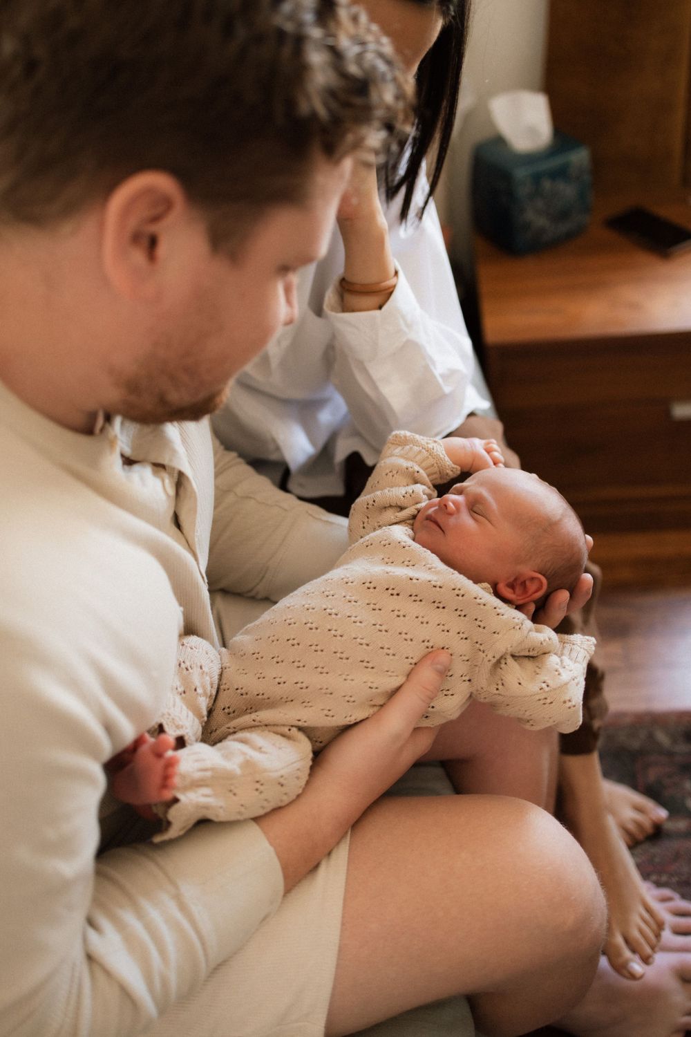 A baby in a knit sweater rests peacefully while being cradled on a lap at home.