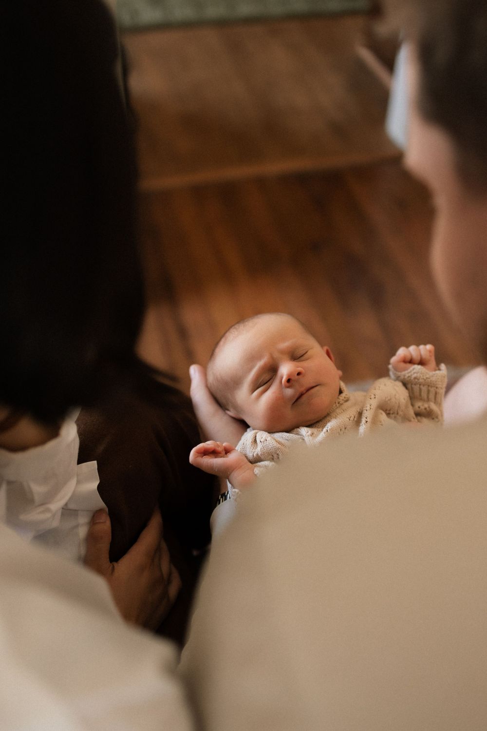 A peaceful newborn baby sleeps while being gently cradled in soft lighting on hardwood floors.