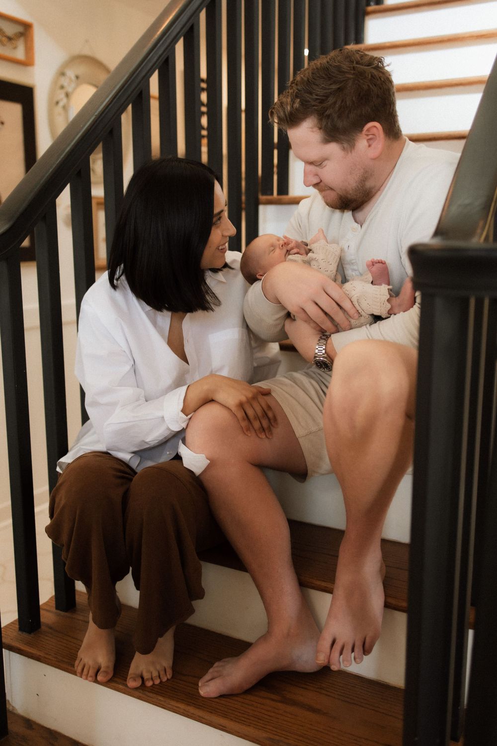 A couple sits on wooden stairs holding their newborn baby in an intimate family moment.