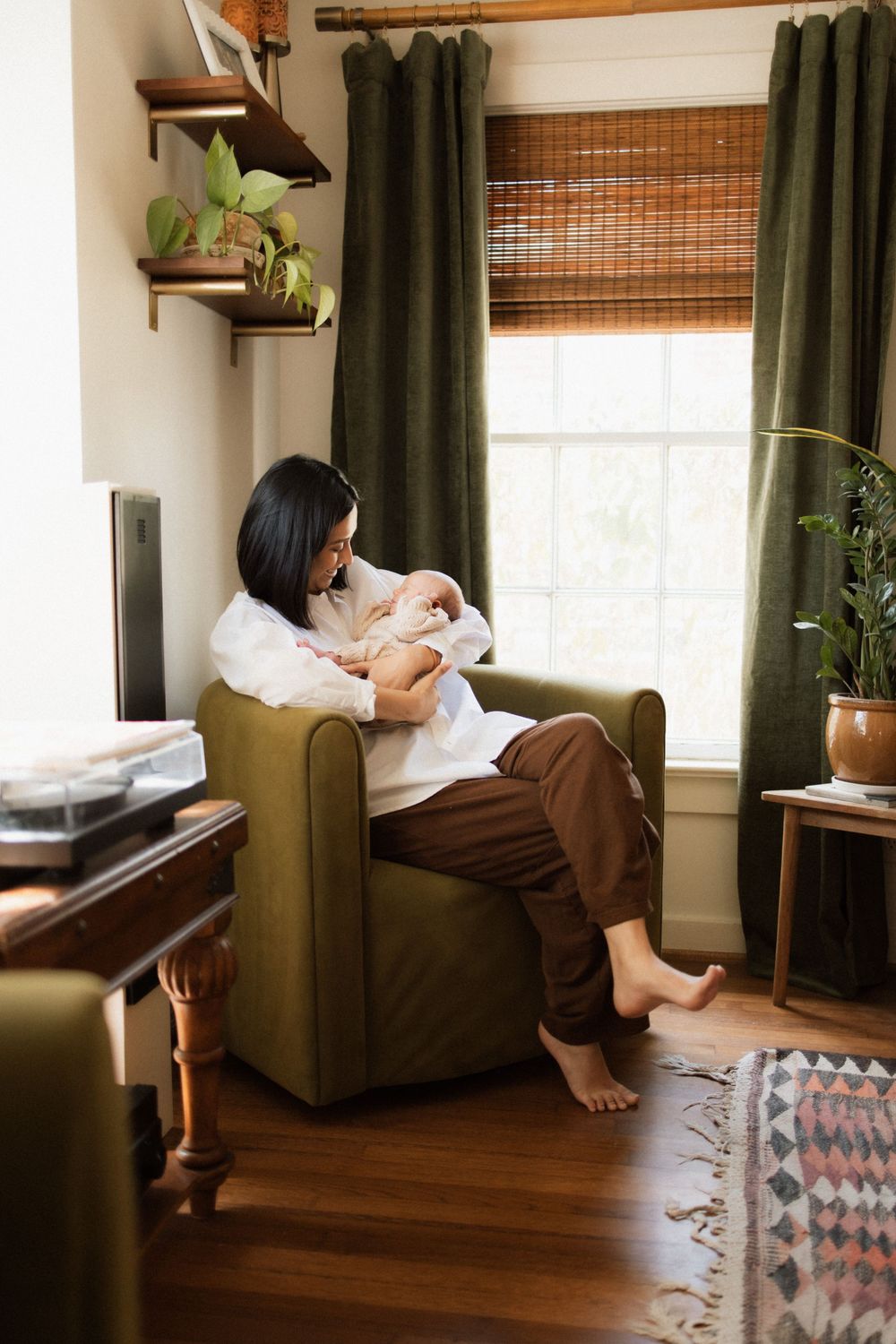 Cozy reading nook with olive green chair, bamboo window shades, and houseplants in a sunlit corner with hardwood floors.
