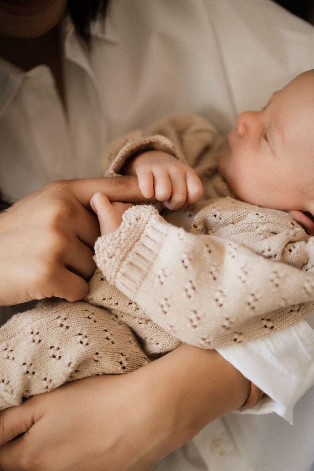 Close-up of sleeping infant in cream knit sweater held in loving arms.