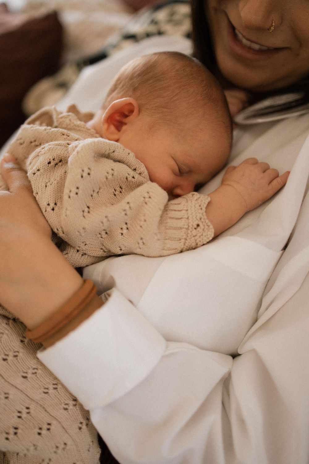 A peaceful sleeping baby wearing a beige knit sweater rests comfortably against soft white fabric.