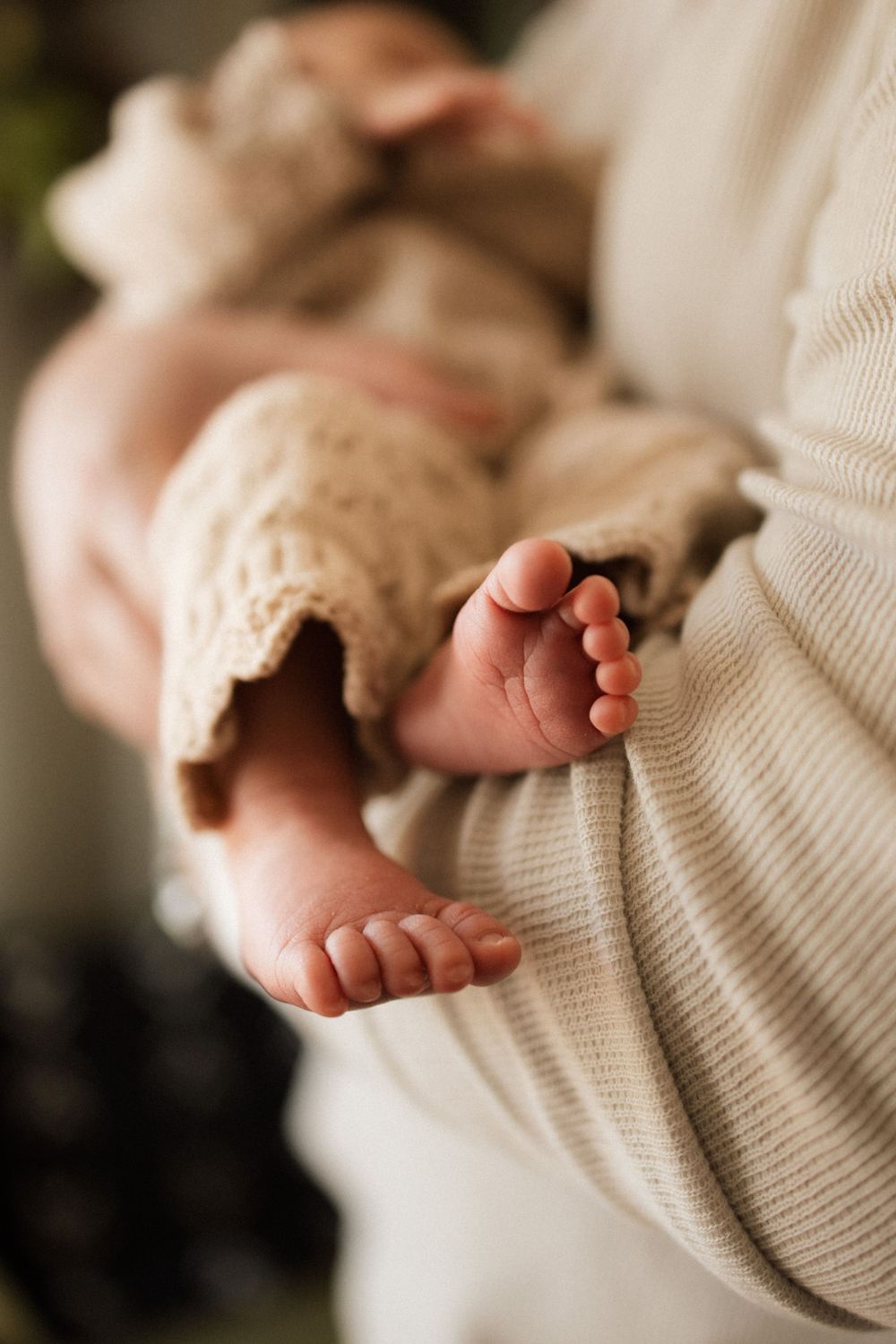 Tiny baby feet peek out from beneath a cozy cream-colored knit blanket.