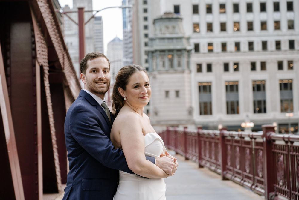 A newlywed couple embraces on an iconic Chicago bridge with classic architecture visible behind them.