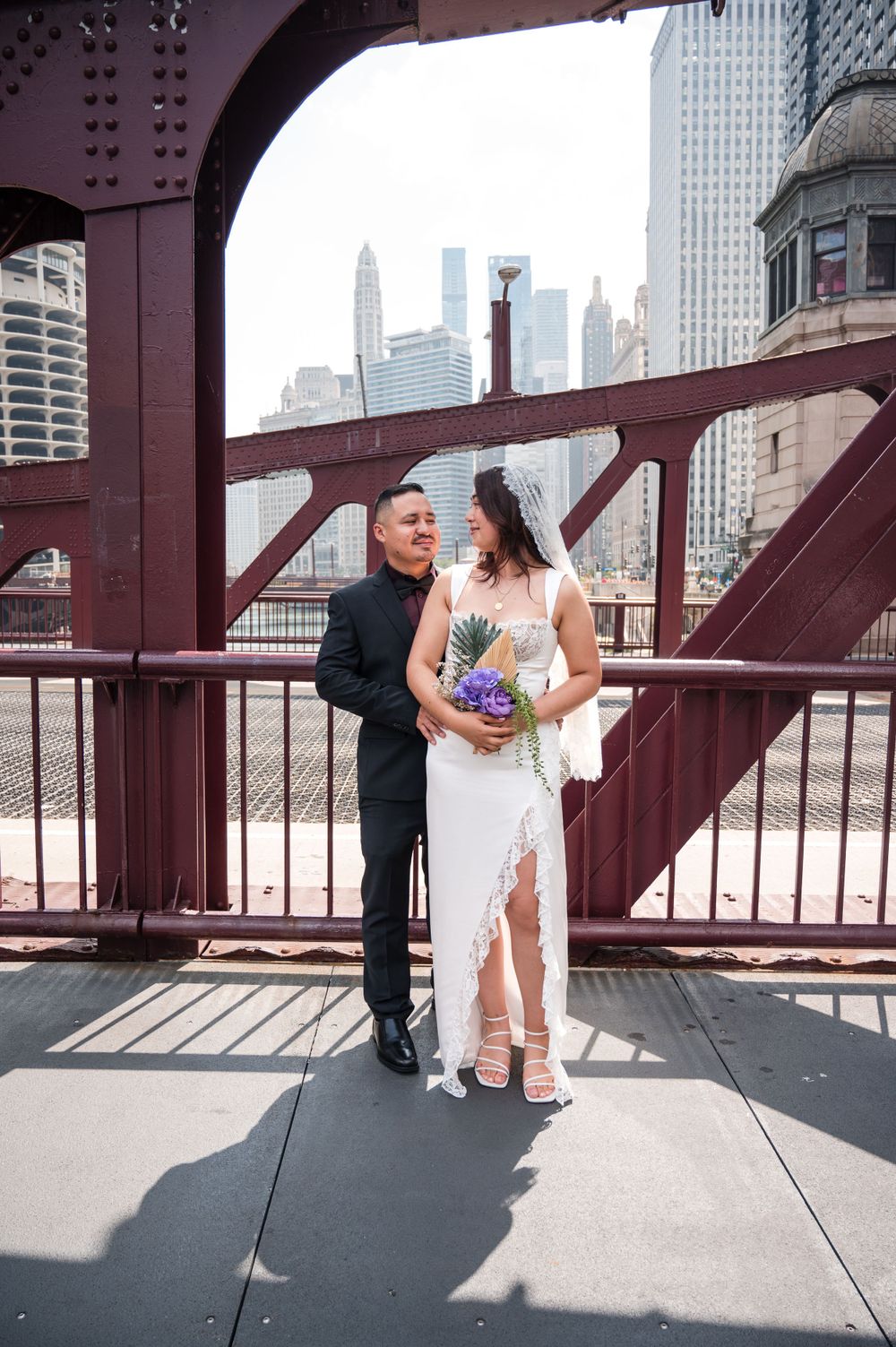 A couple on their wedding day poses on Chicago's iconic red bridge with the city skyline in the background.