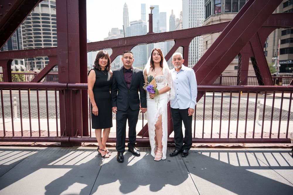 A group of four people stand together smiling on a red bridge with Chicago city buildings in the background.