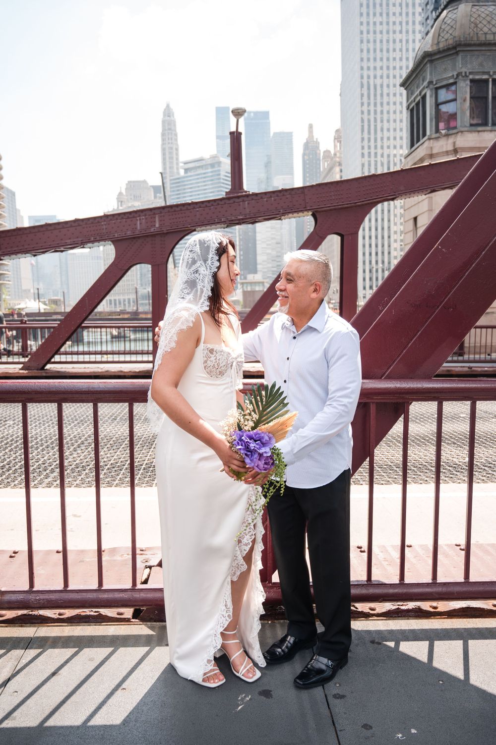 A bride and groom exchange loving looks on an urban bridge with Chicago's skyline in the background.