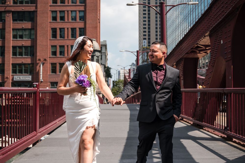 A couple shares a joyful moment while walking across a bright red bridge in an urban setting.