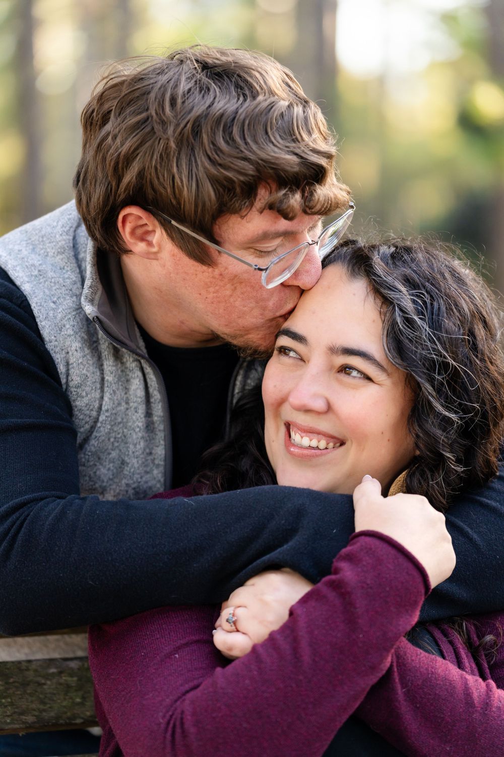 Affectionate couple embracing on wooden bench during outdoor photo session.