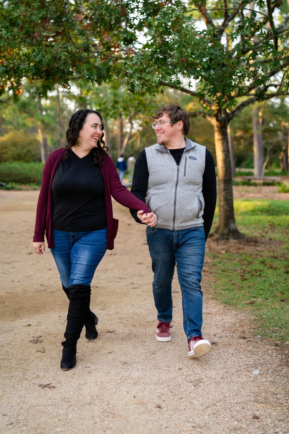 Couple holding hands while walking together on tree-lined path in park.