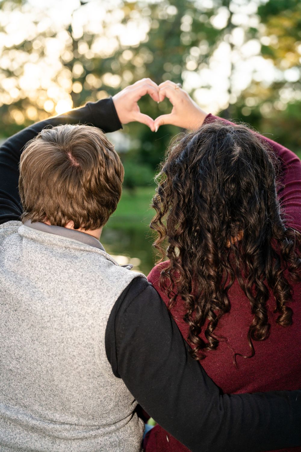 Couple making heart shape with hands against blurred natural background.
