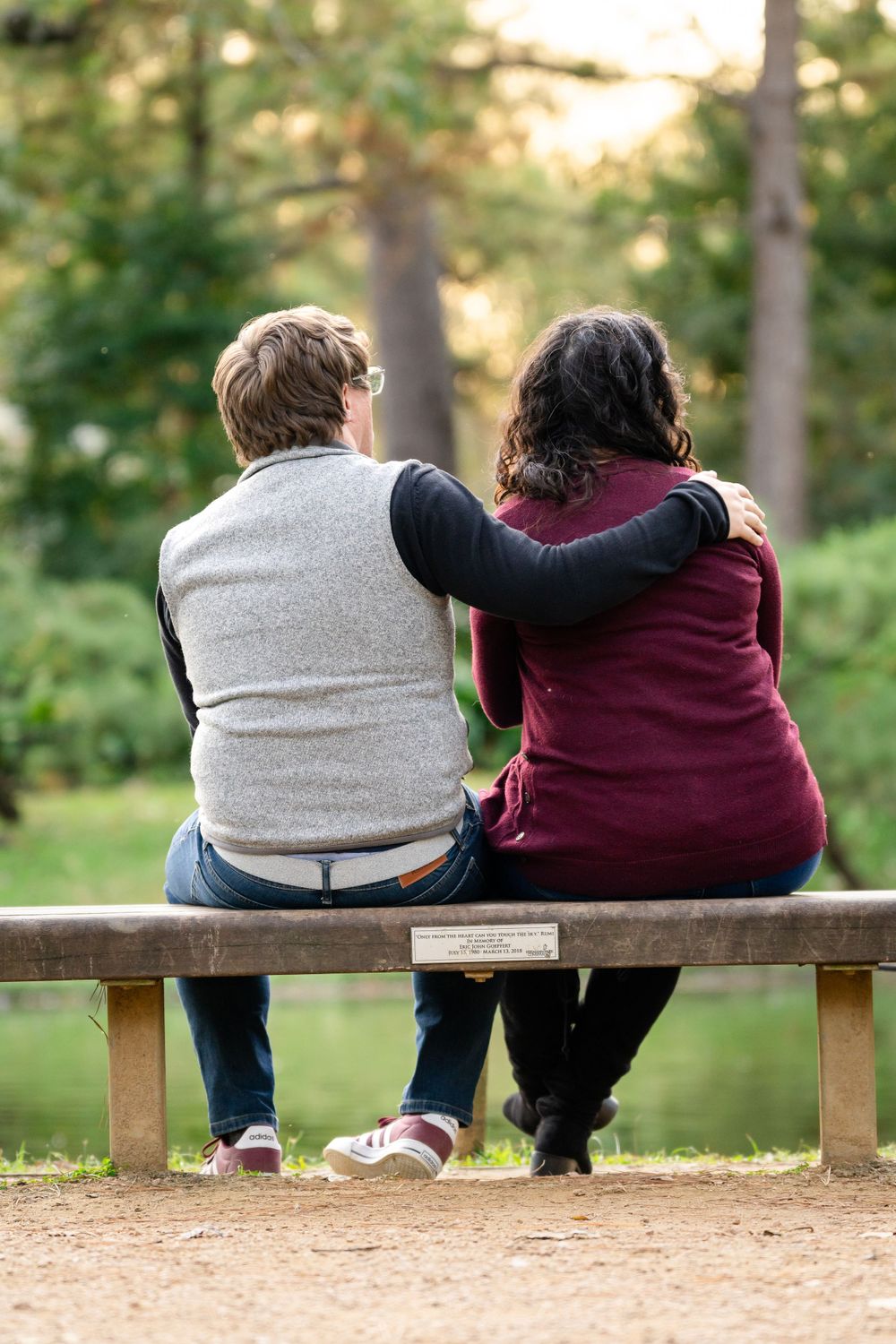 Couple sitting close together on wooden bench overlooking peaceful forest scene.