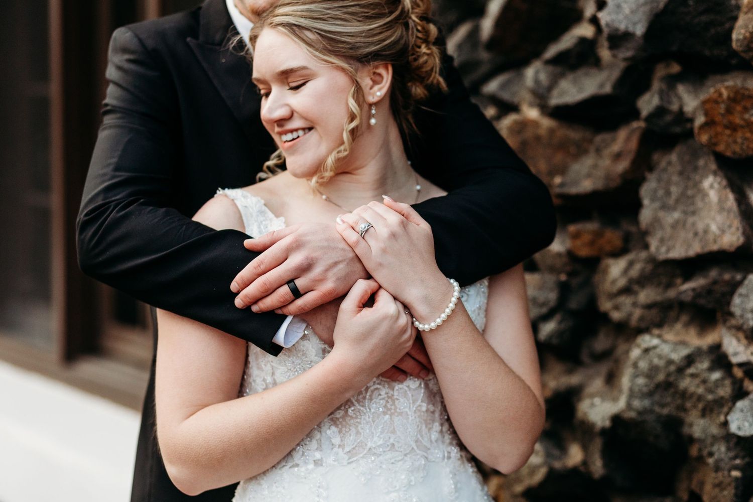 A tender embrace between newlyweds as they share an intimate moment against a stone wall background.