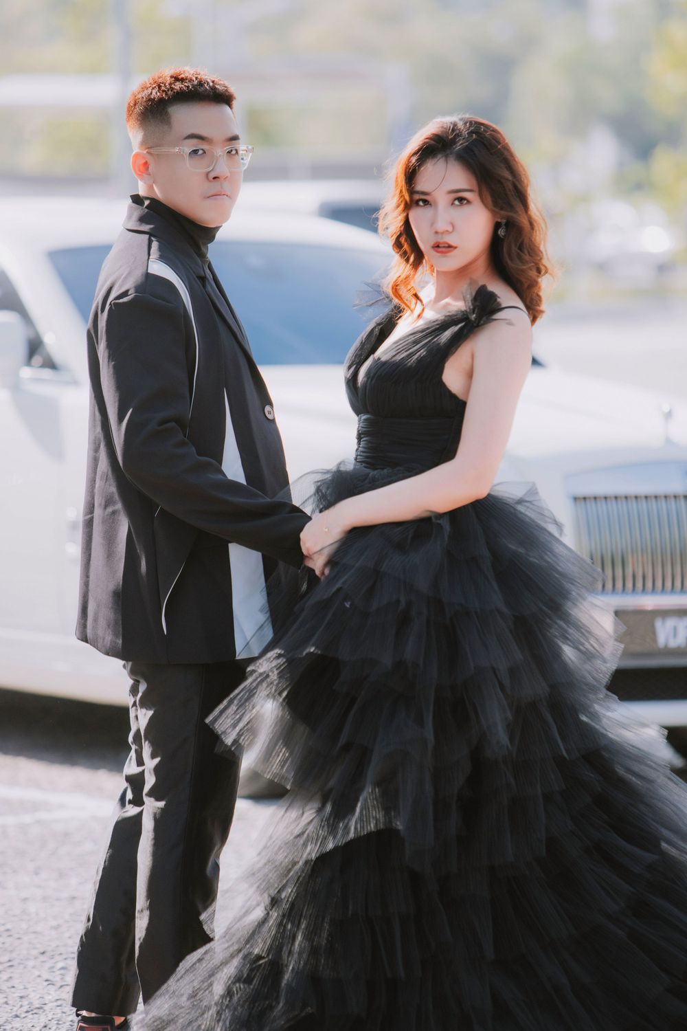 Elegant couple in formal attire posing outdoors, with black tulle gown and sleek suit creating dramatic contrast.