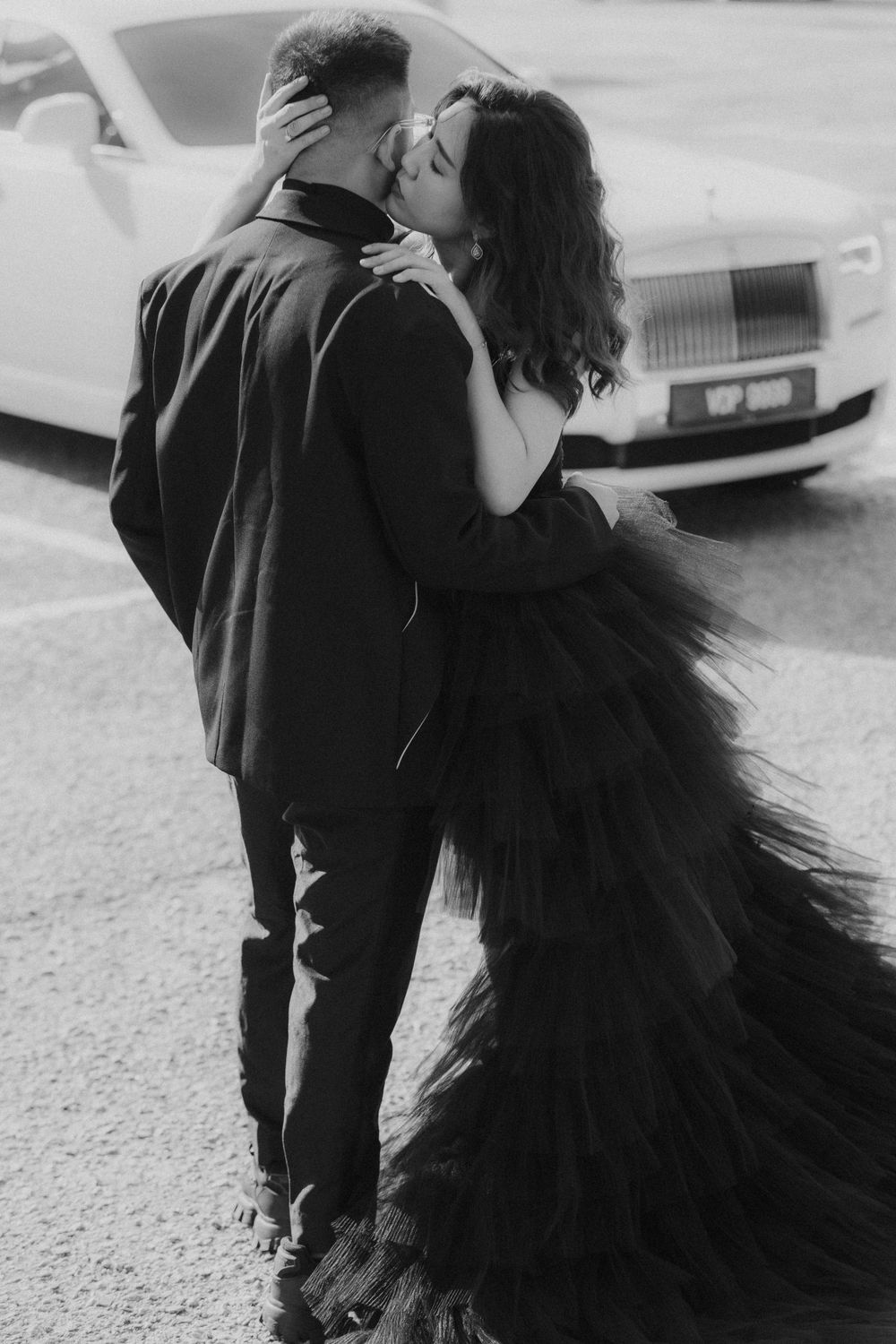 A couple embraces in a romantic black and white photo with the woman wearing a dramatic black tulle gown.