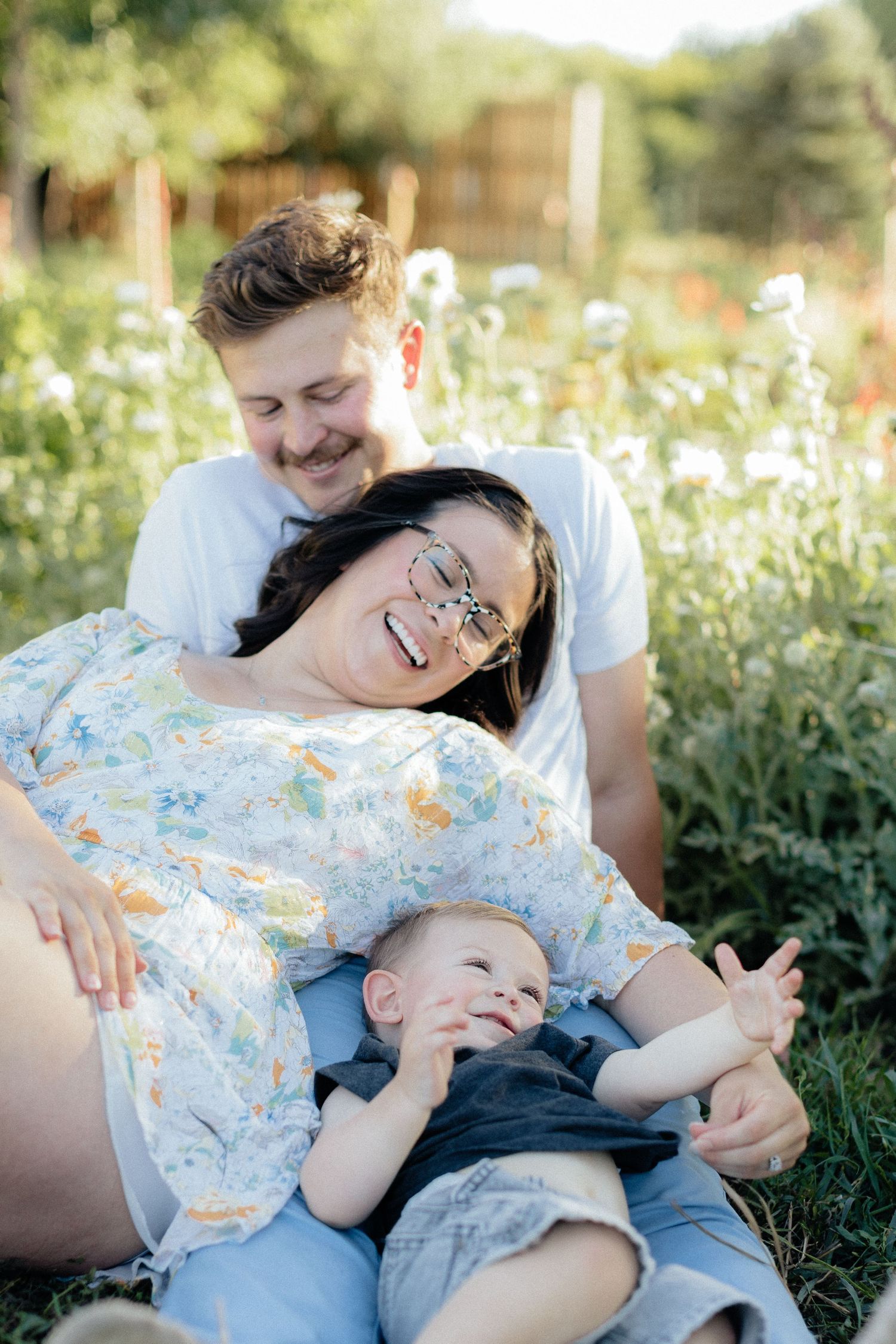 A couple relaxes in a golden autumn field with their baby during a warm sunset photo session.