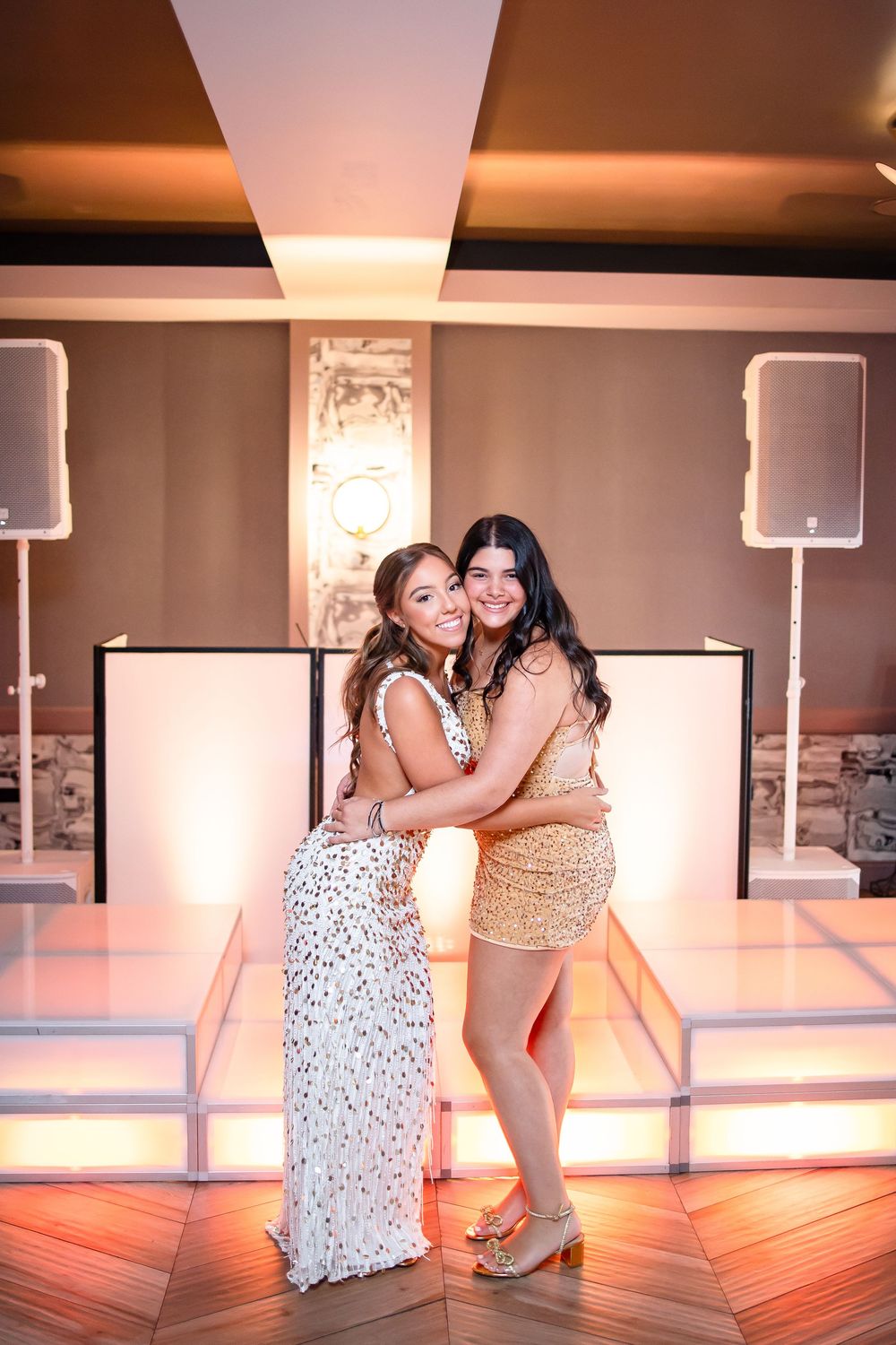 Two dancers in floral and gold dresses perform an intimate contemporary dance sequence in a studio with warm lighting.