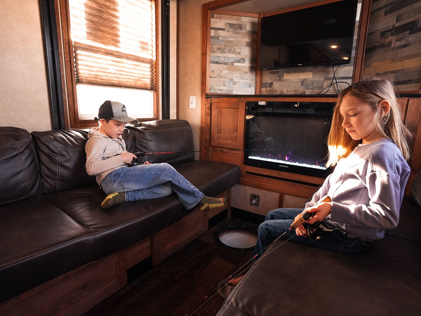 Cozy interior of an RV with people relaxing on leather couches near a fireplace.