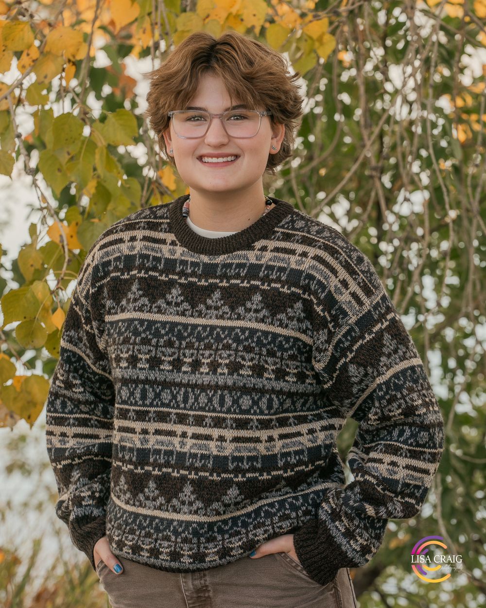 A cozy patterned sweater is worn against a backdrop of autumn leaves.