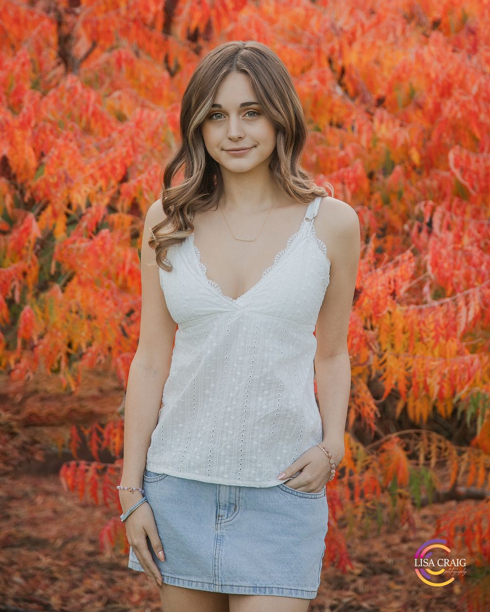 Casual summer portrait in white top and denim skirt against vibrant orange autumn leaves.