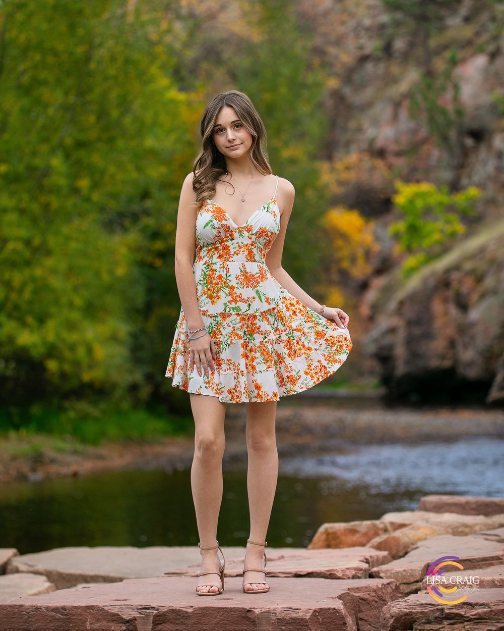 A floral summer dress worn in a scenic outdoor setting with rocks and water in the background.