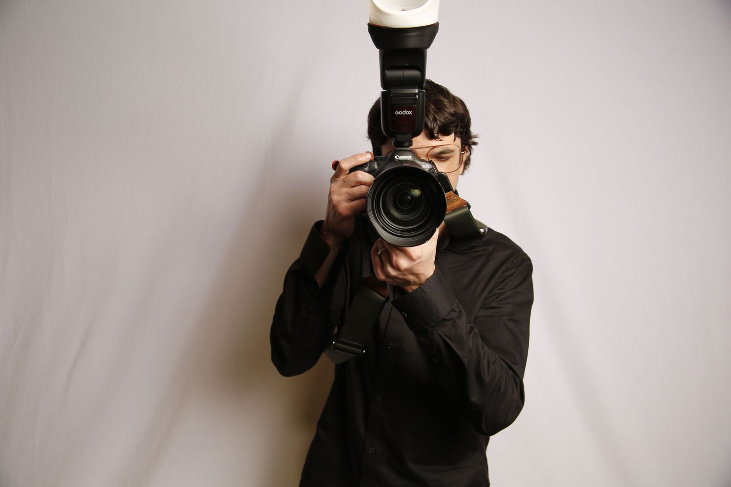 Steven Marsicano Photographer in black attire using professional camera against white background.