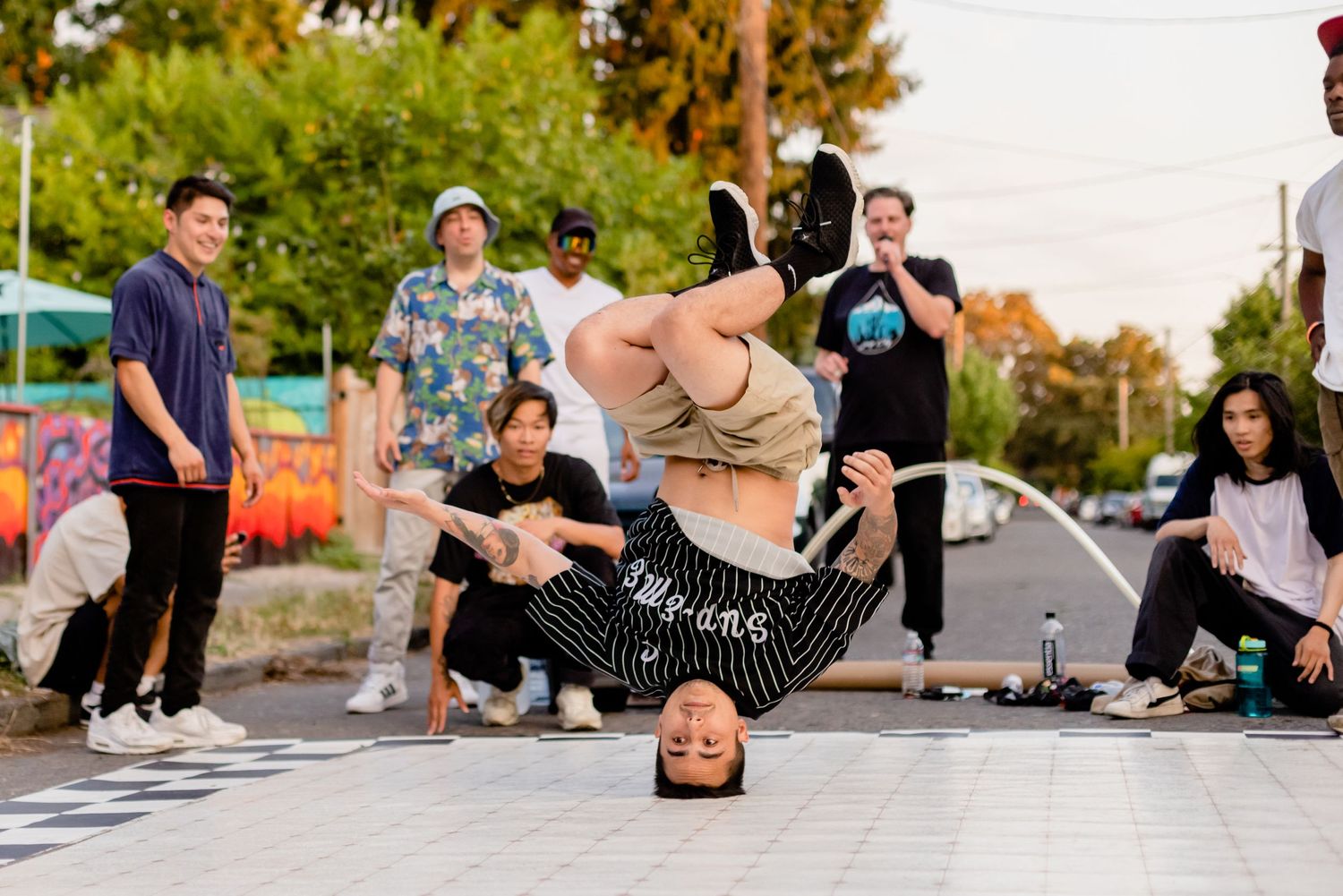 Breakdancer performs an inverted move on concrete while onlookers watch in an outdoor urban setting.