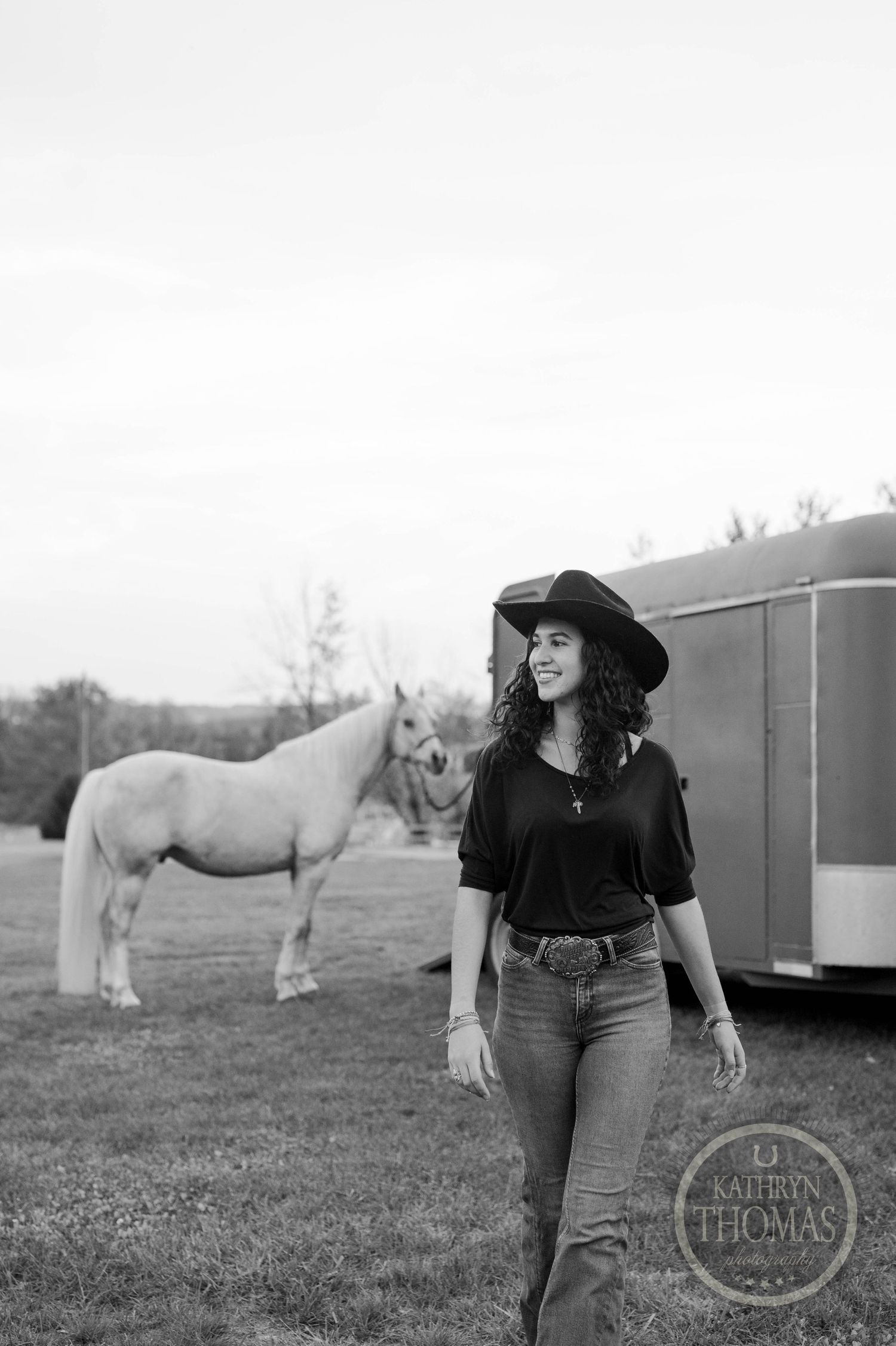 Black and white outdoor scene with a white horse and trailer visible in a pastoral setting.