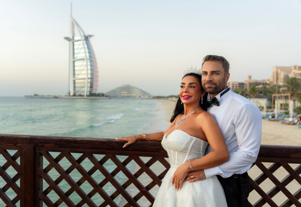 A couple in wedding attire poses at a waterfront view of the Burj Al Arab hotel in Dubai.