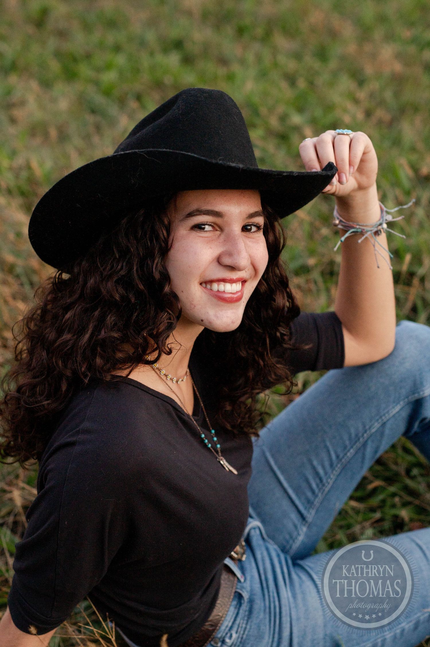 Person in black cowboy hat and denim poses playfully during outdoor photo session.