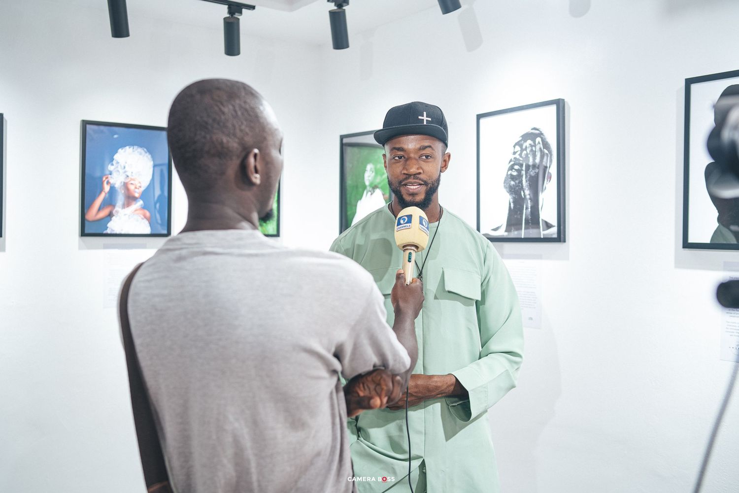 Two people having a conversation in an art gallery with framed portraits on the white walls.