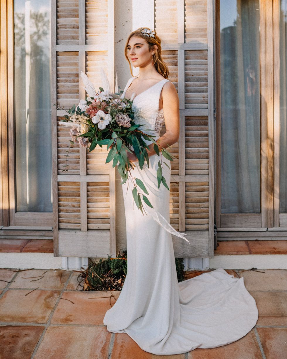 Elegant minimalist bridal portrait showcasing white gown and cascading bouquet against vintage shuttered backdrop.