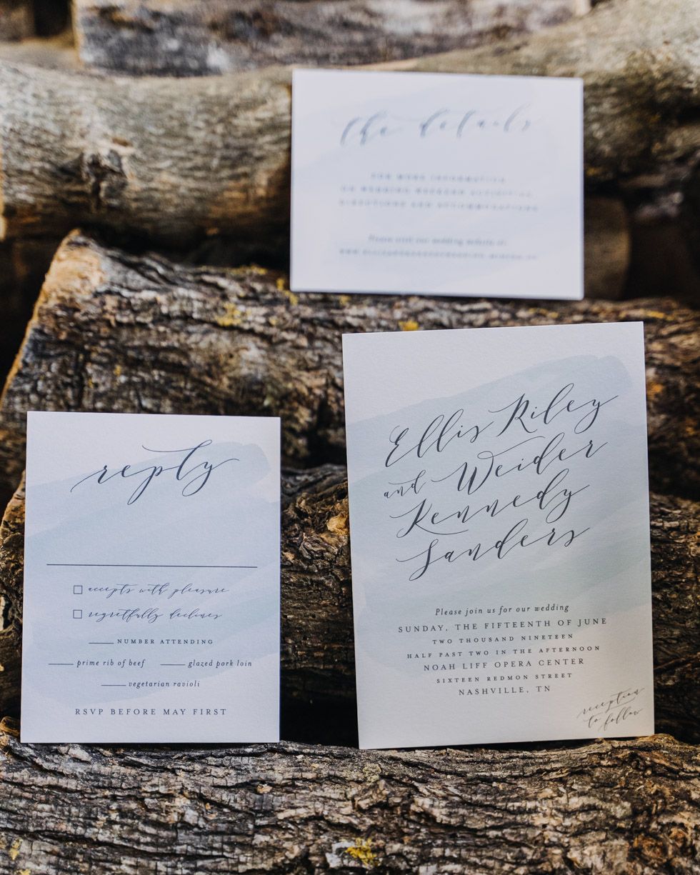 Wedding invitation suite featuring elegant calligraphy on white paper cards displayed on rustic wood texture.