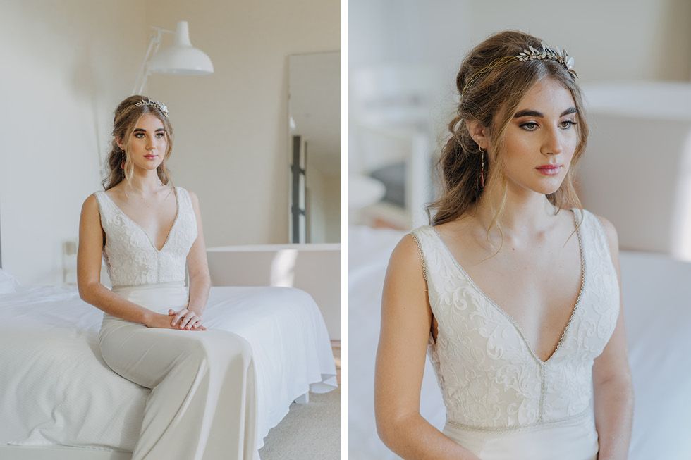 A bride wearing a sleek v-neck lace wedding dress poses in a bright white modern bedroom setting.