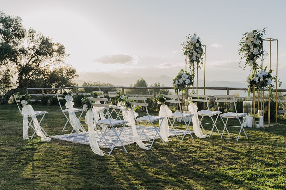 White folding chairs arranged on a grassy lawn at sunset for an outdoor wedding ceremony with scenic views in background.