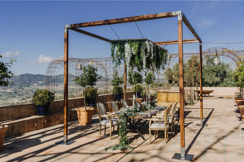 Rustic wooden pergola with hanging plants on a sunny patio overlooking mountain views.
