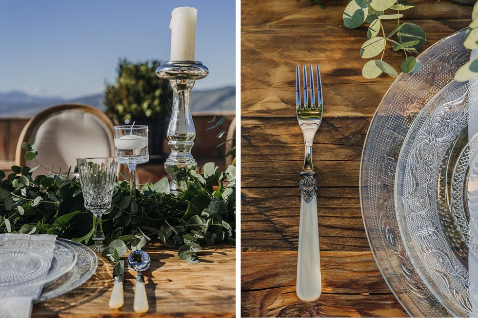 Rustic table setting with silver plates, white candlestick, and eucalyptus greenery on wooden surface in natural light.