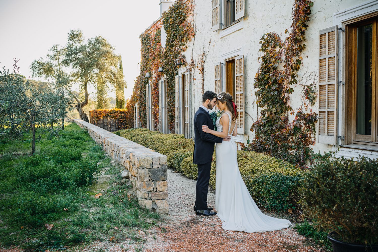 A romantic moment between a couple on their wedding day at a scenic vine-covered estate during golden hour.