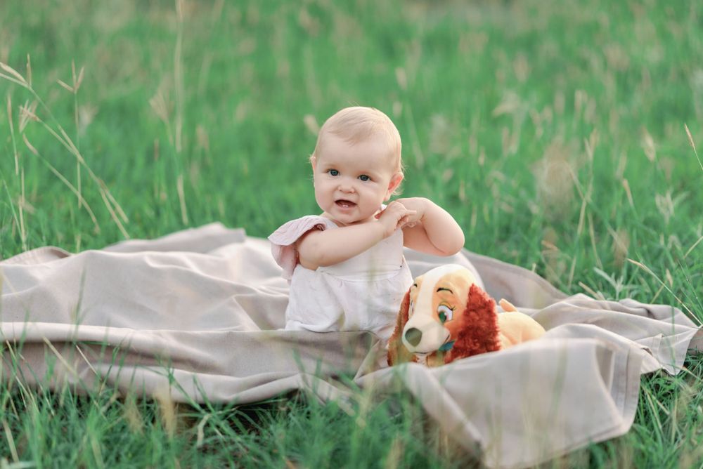 Baby playing with stuffed toy on blanket in green grass.