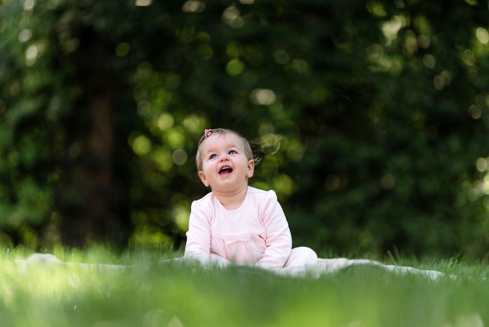 A child in pink clothing plays outdoors in a sunny garden setting with green foliage in the background.