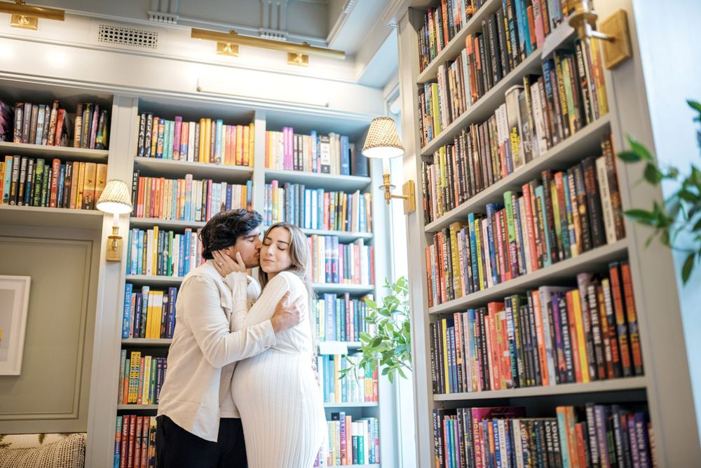 Maternity photoshoot in library with tall bookshelves creating cozy atmosphere.