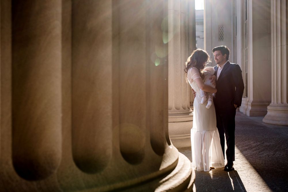 Newlywed couple embraces in warm sunlight between classical stone columns at their wedding.