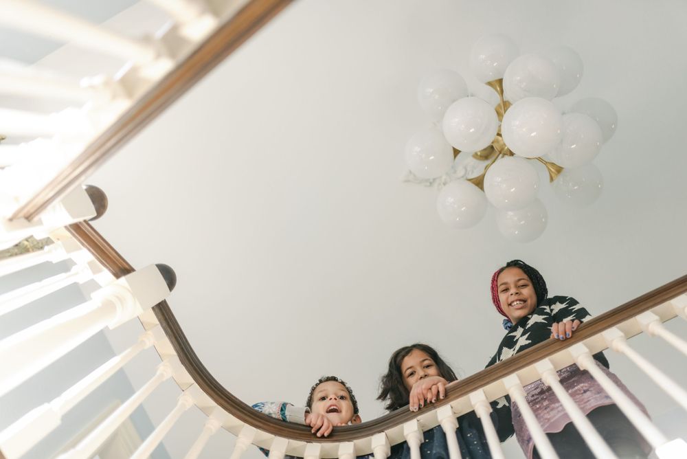 Looking up at smiling faces peering over white staircase railing.