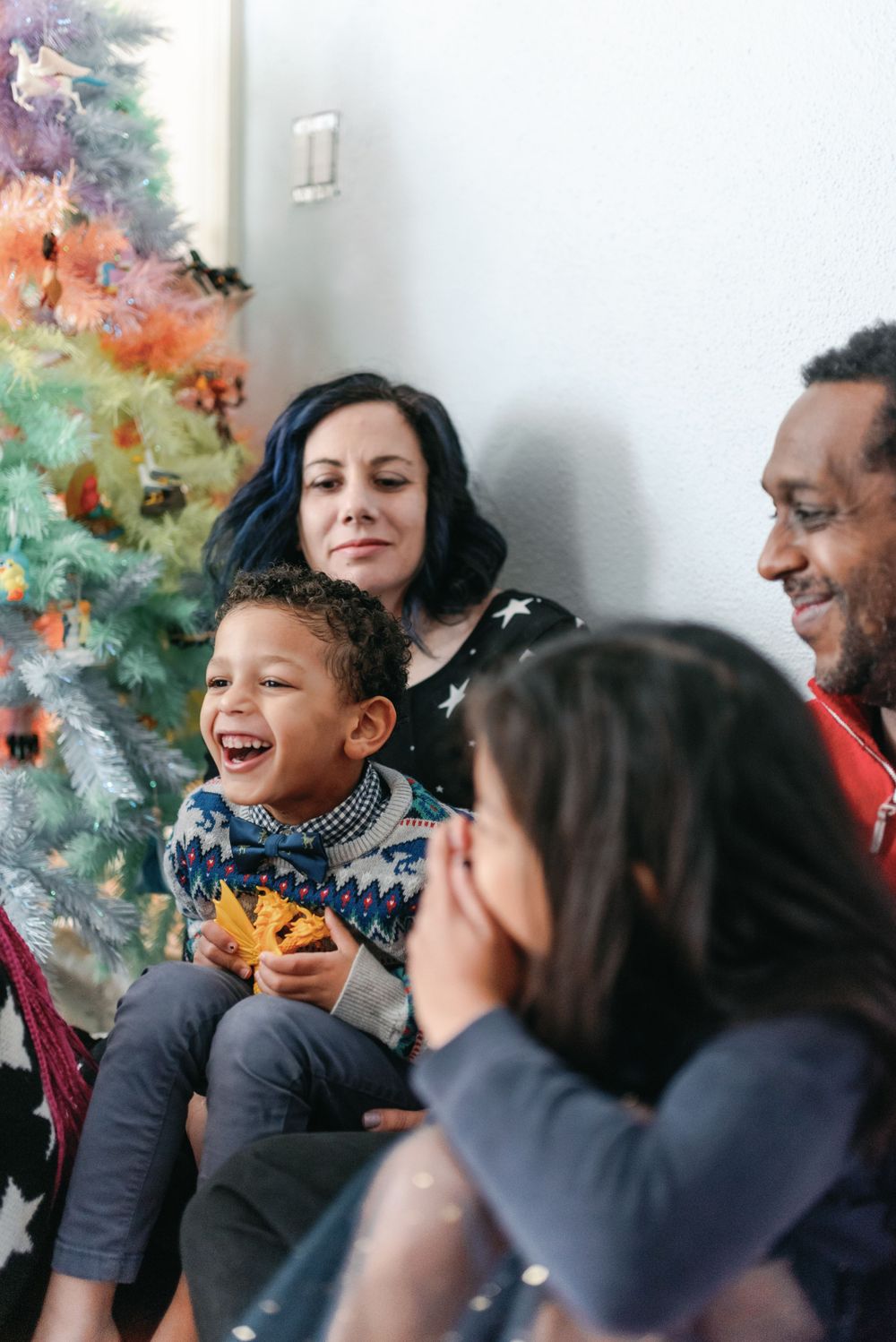 Joyful family moment shared on the floor with laughter and holiday decorations in the background.