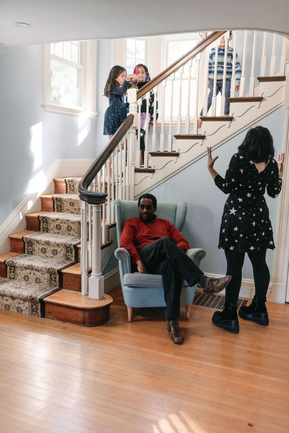Family spreads out across staircase and living room in casual indoor photoshoot.
