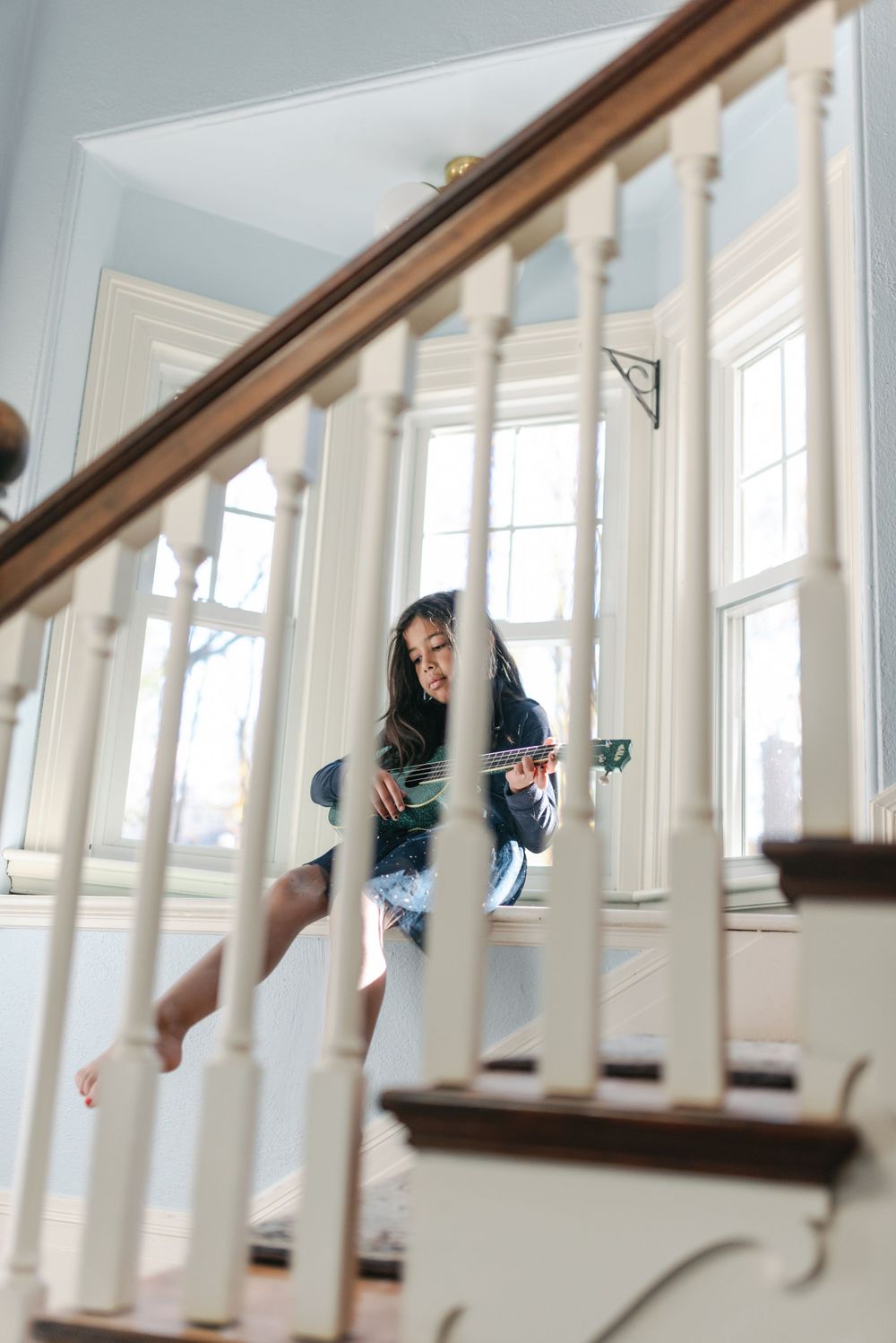 Person sitting on stairs viewed through white banister railings in bright natural light.