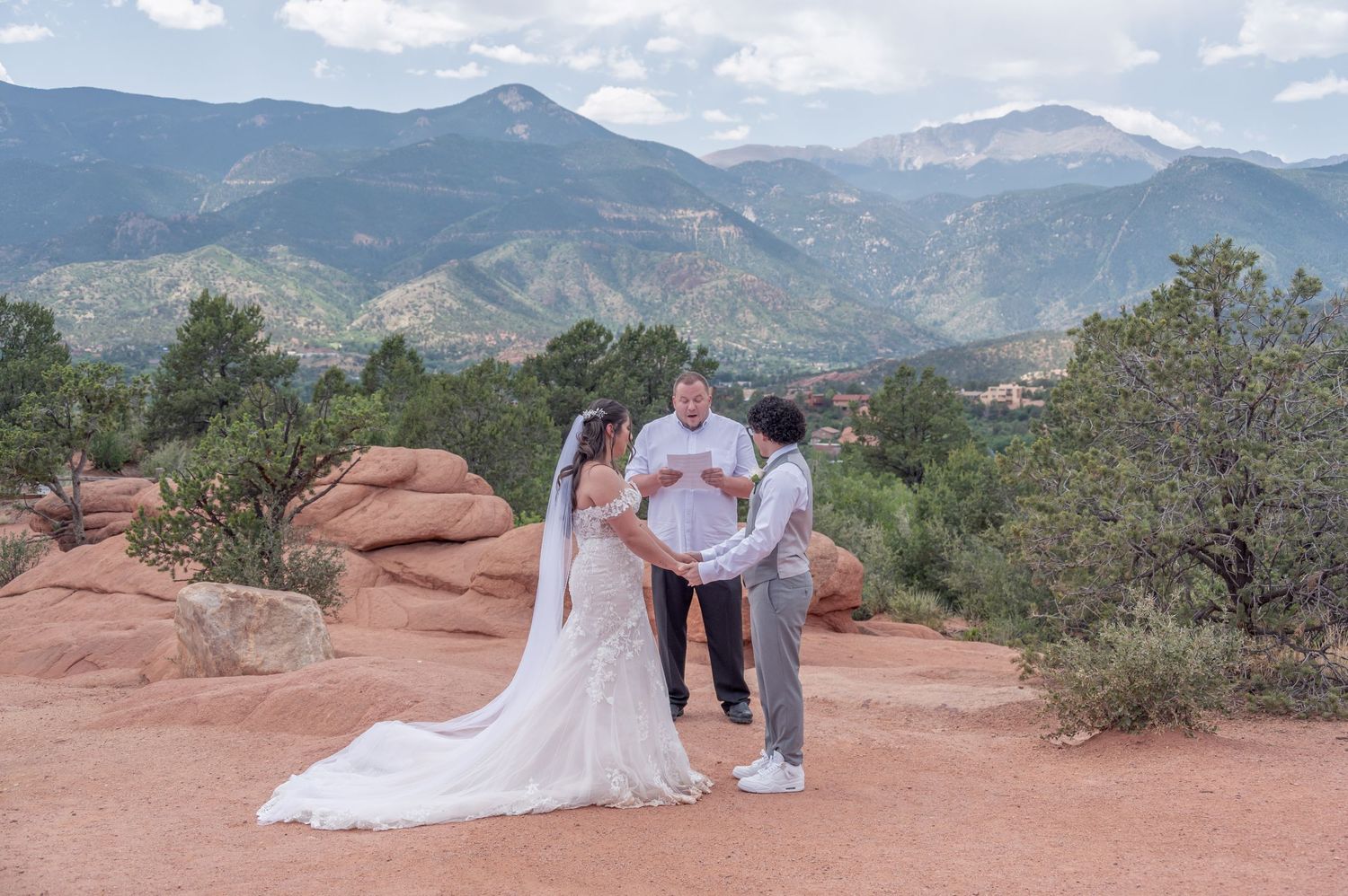 A couple stands on red rocks at Garden of the Gods with mountain views and blue skies in Colorado Springs.