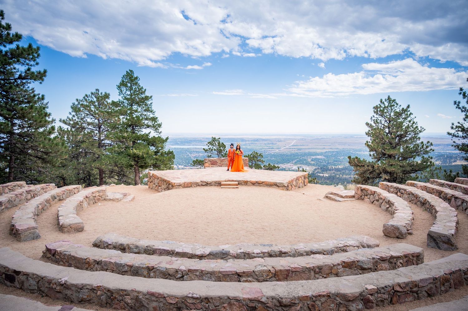 Curved stone amphitheater overlooking mountain vistas with seated viewers enjoying the panoramic Colorado landscape view.